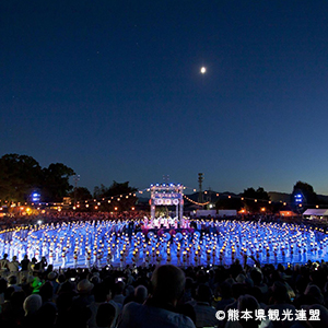 月の下、浴衣姿の女性たちが青く光り円を描いている幻想的なまつりの写真