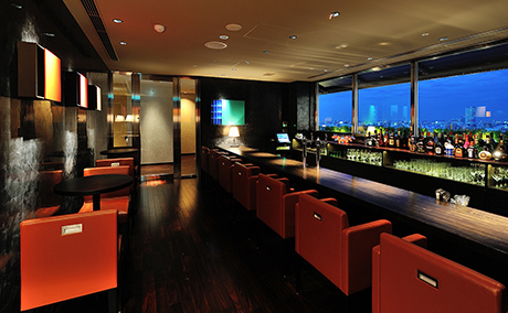 オレンジ色の椅子とカウンター、2人用のテーブル席がある、バーの写真