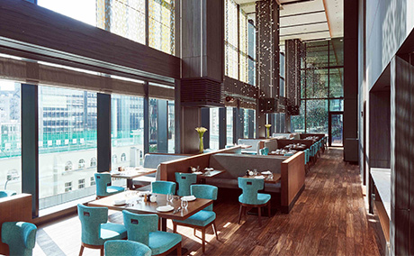 レストラン Anchor Tokyo。茶色いテーブルと水色の椅子が並び、高い天井からは葉っぱのような装飾が吊り下げられている写真