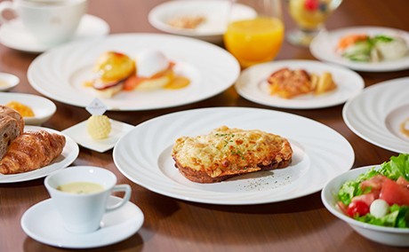 クロックムッシュをメインに、クロワッサン、サラダ、オレンジジュースなど豪華な朝食が並んでいる写真